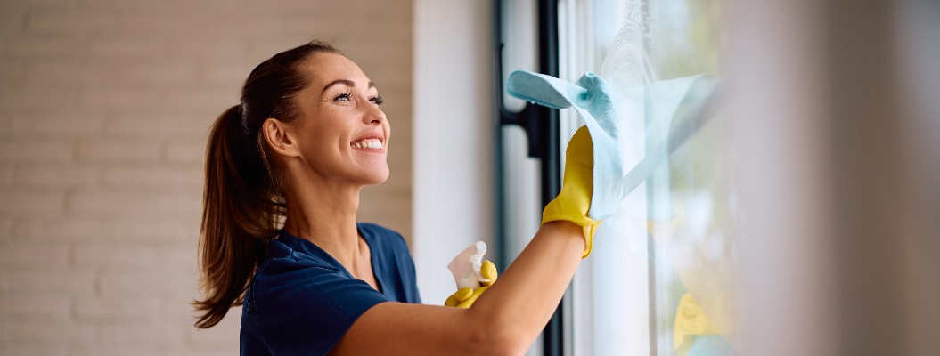 Junge, zufriedene Frau, die zu Hause Fenster putzt. Freiraum.