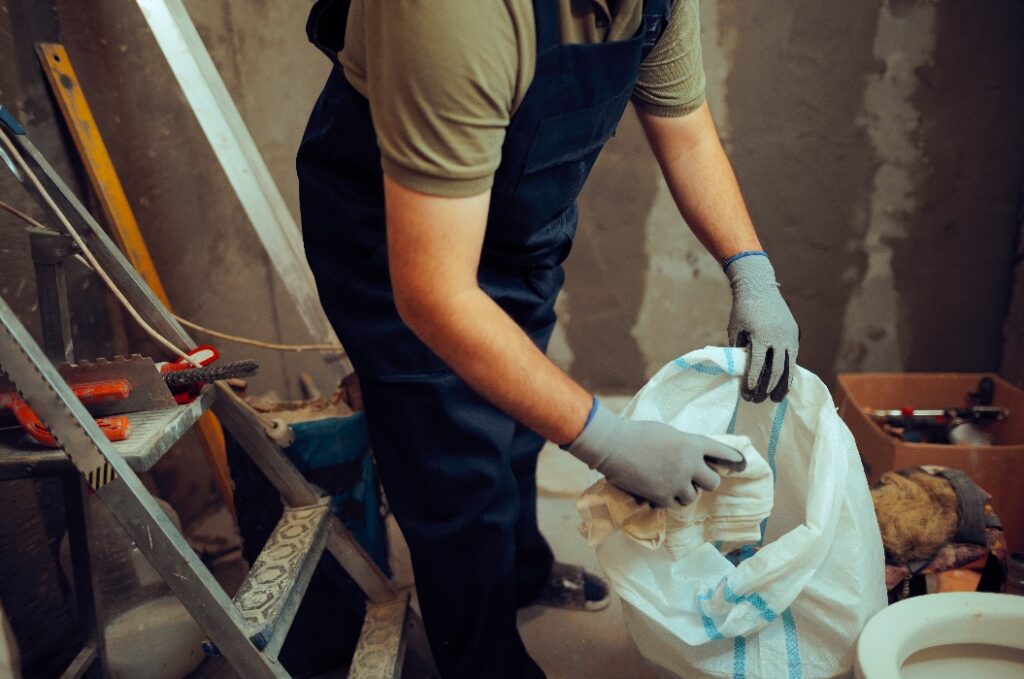 Ein Bauarbeiter sammelt Müll in einem Müllsack auf der Baustelle ein. Ein Handwerker räumt einen unordentlichen Arbeitsbereich auf